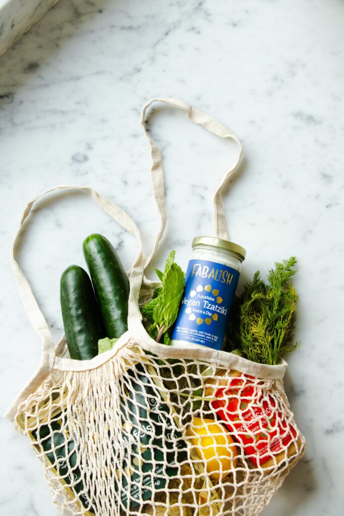 Knitted carrier bag with fresh ingredients inside on top of a white marble worktop.